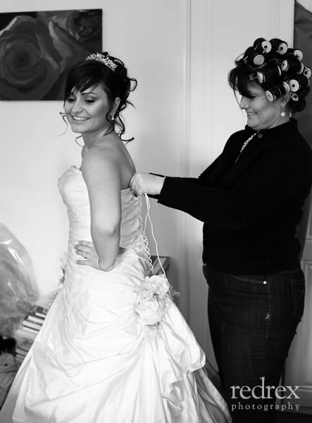 Bride getting into wedding dress with help from Mother